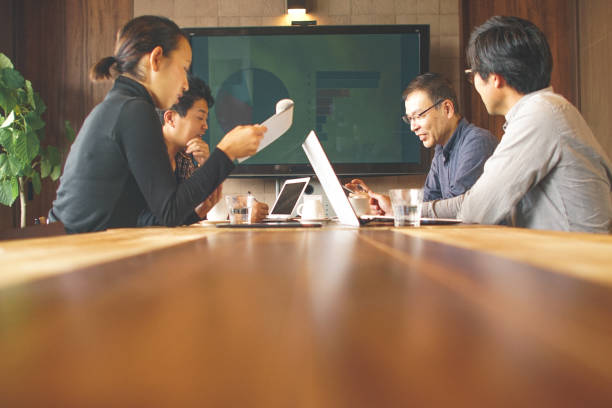 A long wooden conference table leading to a blurred background of a business team actively collaborating.