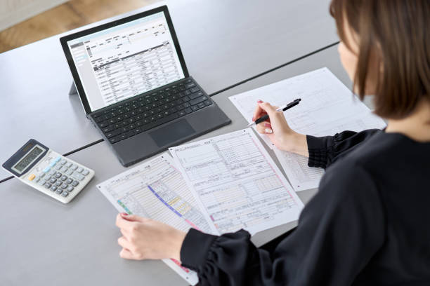 A businesswoman sitting at a desk analyzing printed charts and graphs next to an open laptop and calculator.